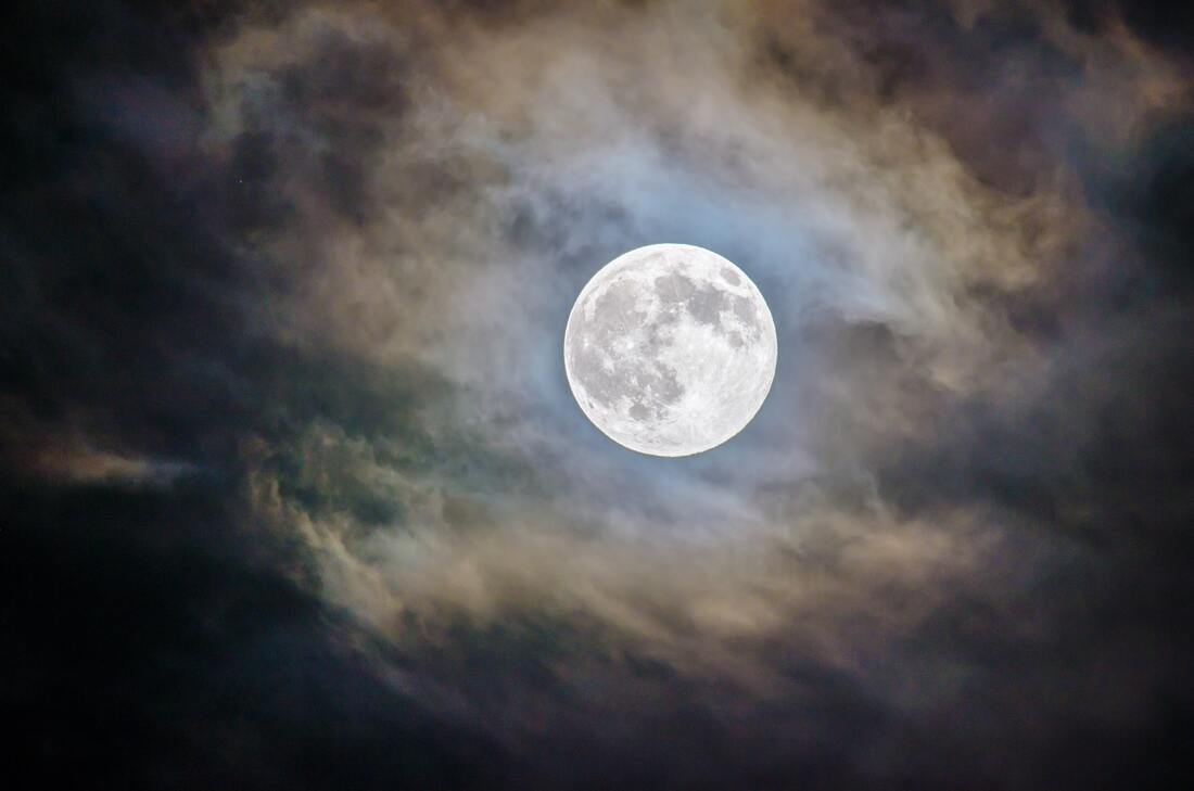 A picture of a full moon surrounded by clouds.